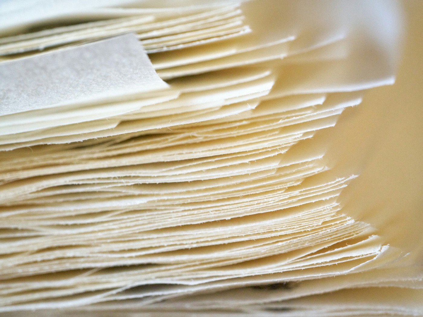 Canto de un bloque de hojas de papel de algodón, con la luz rasante marcando una a una las capas