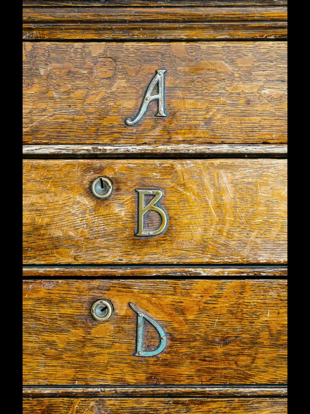 Tres cajones de roble, uno sobre otro, con las letras A, B y D en latón descendiendo por la madera