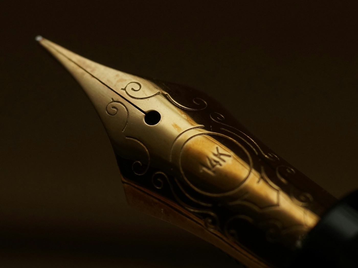 Plumín de oro de una pluma de autor, con grabado fino, sobre un fondo cálido en penumbra